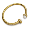 Bracelet jonc ouvert doré pour femme avec deux perles blanches décoratives aux extrémités et détails brillants incrustés sur le contour du bijou.