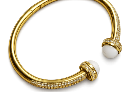 Bracelet jonc ouvert doré pour femme avec deux perles blanches décoratives aux extrémités et détails brillants incrustés sur le contour du bijou.