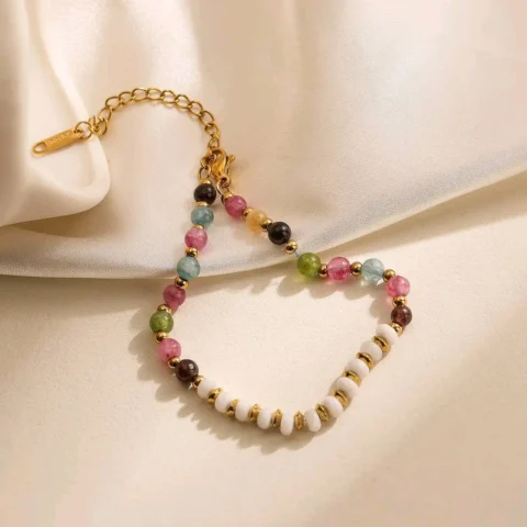 Bracelet femme haut de gamme en pierres naturelles pastel multicolores avec perles blanches et finitions dorées, présenté sur un tissu satiné beige.