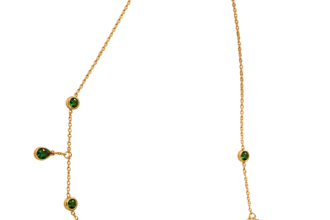 Collier doré pour femme avec chaîne fine ajustable, pampilles suspendues et éléments décoratifs verts, présenté sur un fond beige élégant.
