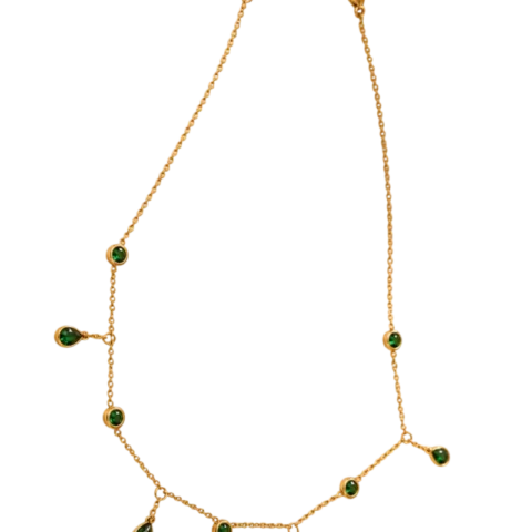 Collier doré pour femme avec chaîne fine ajustable, pampilles suspendues et éléments décoratifs verts, présenté sur un fond beige élégant.