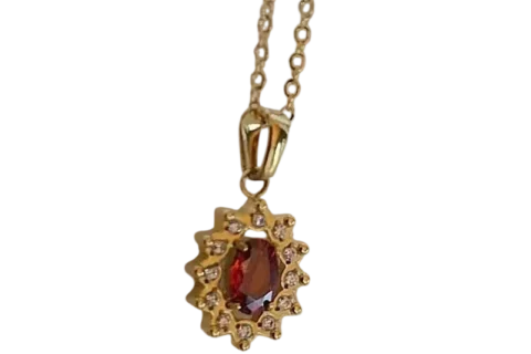 Collier doré pour femme avec pendentif composé d'une pierre rouge ovale entourée d'un halo de petites pierres scintillantes, au style élégant et raffiné.
