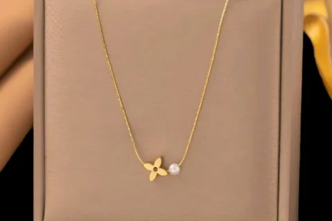 Collier femme doré avec chaîne fine, pendentif trèfle à quatre feuilles et perle blanche au design élégant et minimaliste.