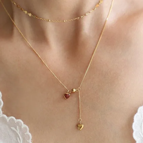 Collier en acier inoxydable doré avec deux pendentifs en forme de cœur, dont un cœur rouge et une chaîne pendante élégante.