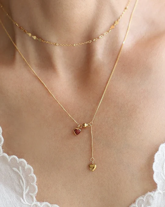 Collier en acier inoxydable doré avec deux pendentifs en forme de cœur, dont un cœur rouge et une chaîne pendante élégante.