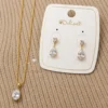 Ensemble de bijoux doré pour femme comprenant un collier avec pendentif en forme de goutte et des boucles d'oreilles pendantes assorties ornées de pierres transparentes.
